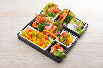 Bento meal of rice, salmon, broccoli, lettuce and noodle on wood