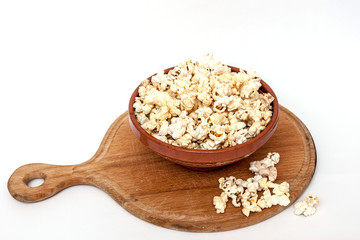 Wooden cutting board, clay bowl full of popcorn, some  scattered