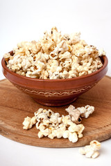 Wooden cutting board, clay bowl full of popcorn, some  scattered