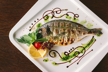 Fried snapper fish with lemon and herbs on white plate