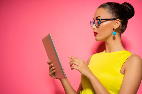 Youth and technology. Colorful studio portrait of young attractive brunette woman using tablet computer against pink wall.