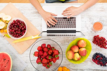 A beautiful mature woman using a Laptop computer in the kitchen with fruits..
