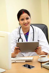 Traditional female doctor holding tablet computer at clinic desk - 121016413