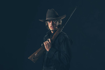 Retro 1900 western cowboy standing with rifle. Young man. Studio