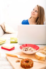 A young woman having breakfast while using a laptop computer..