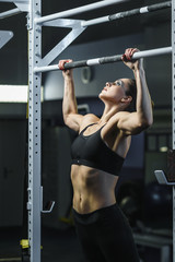 Fototapeta na wymiar Concept: power, strength, healthy lifestyle, sport. Powerful attractive muscular woman CrossFit trainer do pull ups during workout at the gym