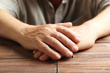 Hands of old senior on a wooden table