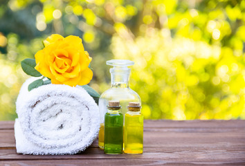 Fototapeta na wymiar Massage oil, white towel and flower elixirs. Cosmetics for saunas and spa treatments. Spa concept. Essential oils. Cosmetics for saunas and spa treatments. Fragrant yellow rose. Copy space. 