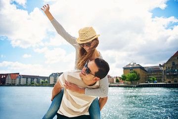 Fun loving young couple frolicking at a waterfront - obrazy, fototapety, plakaty