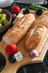 Two bread baguettes and ingredients on wooden cutting board