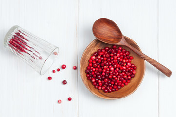 Top flat view: cranberries in wooden bowl with spoon and glass on white surface