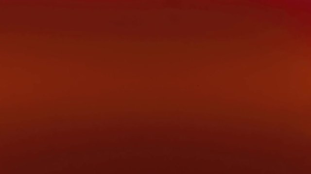 The black silhouette of a vintage toy car moving aorund on a mirror surface. Red background. Macro close-up shot.
