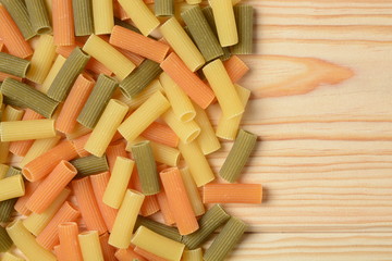 Pasta macarrones en froma de tubo de tres colores cruda sobre un fondo de madera