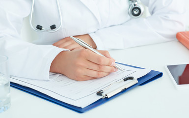 Female medicine doctors hands filling patient medical form.