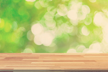 green bokeh leaves and wood table background with sunlight.