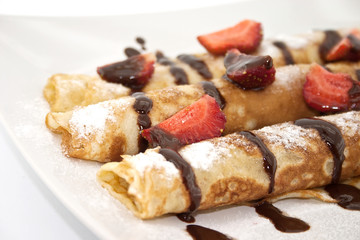 Sweet dessert of rolled pancakes on a plate with strawberry