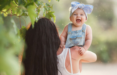 Young woman brunette with long straight hair,wearing a white shirt and blue shorts,holding his little daughter,dressed in blue jumpsuit,a family walking in summer green Park