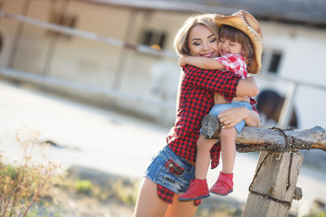 Happy young mother,spends time in the village in the summer with her daughter,a little girl with blond hair and mother and daughter, dressed in a Red plaid shirt and blue denim shorts