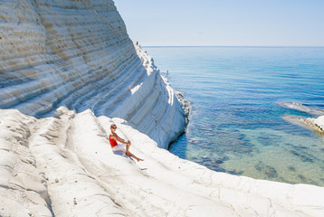 A girl sits on a slope of white cliff called "Scala dei Turchi"