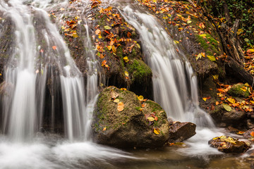 Fototapeta na wymiar Beautiful waterfall with fallen leaves in the autumn