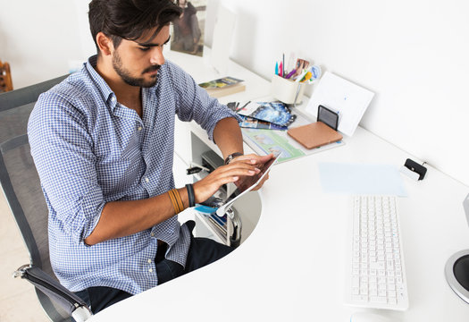 Portrait of male designer using computer and tablet in a bright office.