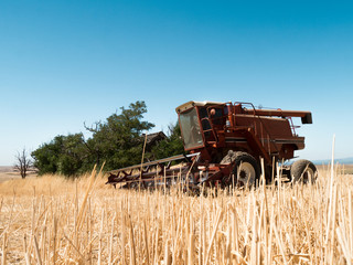 Red harvester idling in straw field after work is done