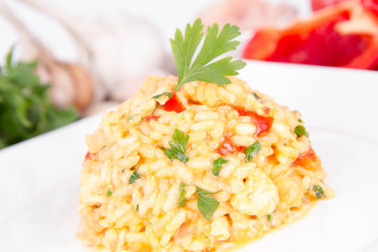 Risotto with chicken, tomatoes, bell pepper, onion, parsley and garlic on a white plate on a wooden background