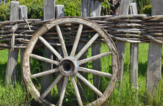 Closeup of an old wheel of a traditional cart leaning on a wooden fence