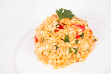 Risotto with chicken, tomatoes, bell pepper, onion and garlic on a white plate decorated with parsley 