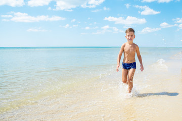 Fototapeta na wymiar Cute little boy running through the water at beach