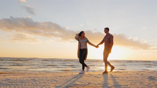 Steadicam slow motion shot: Romantic couple walking on the beach at sunset, holding hands, having a good time