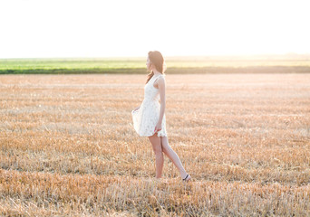 Fototapeta na wymiar Portrait of beautiful young woman walking through a wheat field at sunset.