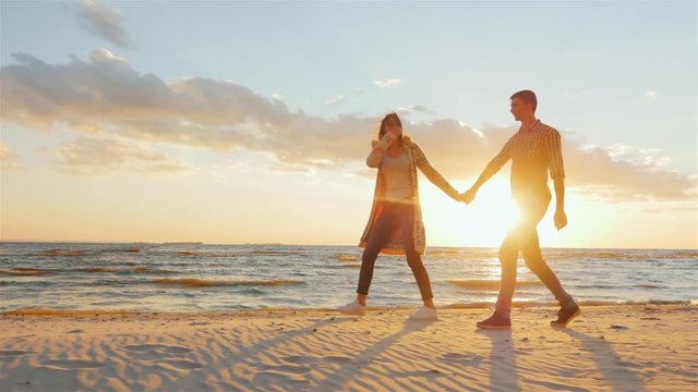 Steadicam shot: Loving couple walking at sunset on the beach or lake. She leads the guy flirting