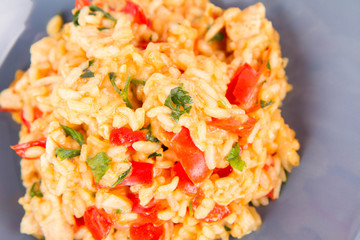 Risotto with chicken, tomatoes, bell pepper, onion, parsley and garlic on a blue plate on a wooden background