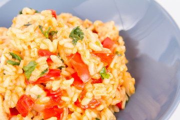 Risotto with chicken, tomatoes, bell pepper, onion, parsley and garlic on a blue plate on a wooden background