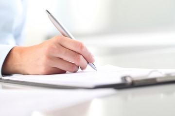 Woman's hands writing on sheet of paper in a clipboard and a pen - obrazy, fototapety, plakaty