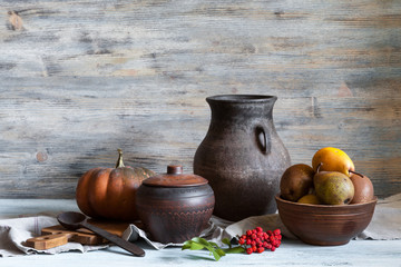 Still life in a rustic style: a set of pottery, pumpkin and pears. Natural light from window.