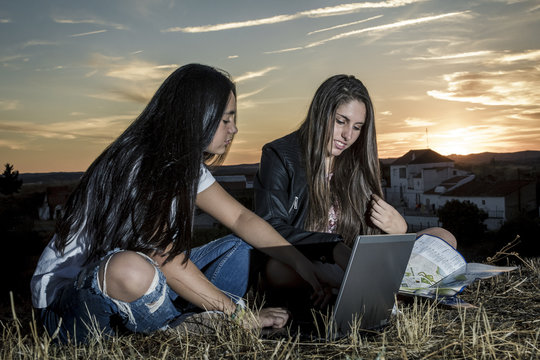 J&oacute;venes amigas con su ordenador port&aacute;til chateando en la monta&ntilde;a al lado del r&iacute;o al atardecer. Chicas viajeras explorando nuevos caminos. Un mundo conectado.