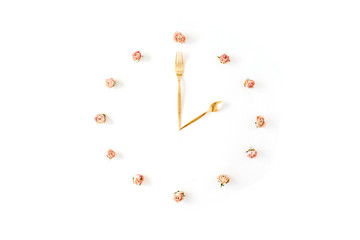 flat lay clock face made of rose buds, spoon and fork. top view