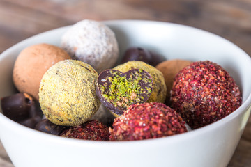 Colorful dessert, raw vegan sweets and organic chocolate in a bowl on a wooden background, close-up.