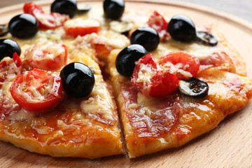Sliced delicious pizza on wooden plate, close up