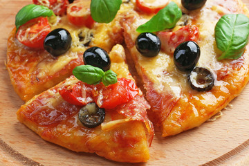 Sliced delicious pizza with olives on wooden plate, close up