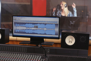 Young woman recording a song in a professional studio. View from sound engineer workplace