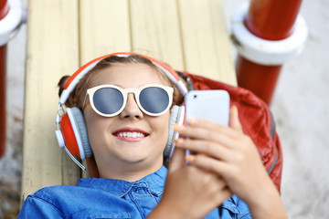 Cute young girl lying on bench in playground and listening music