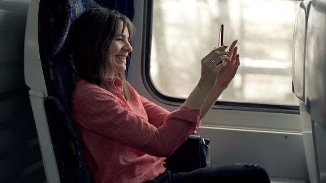 Young woman taking selfie photo with cellphone sitting on train 
