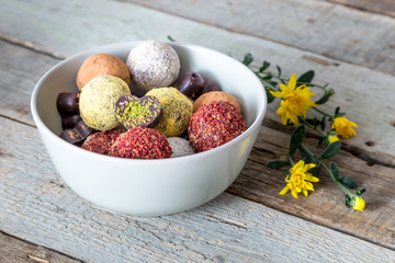 Colorful dessert, raw vegan sweets and organic chocolate in a bowl on a wooden background decorated with chrysanthemum flowers for autumn mood 
