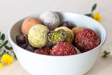 Colorful dessert, raw vegan sweets and organic chocolate in a bowl on a wooden background decorated with chrysanthemum flowers for autumn mood 