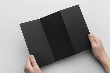 Black A4 Z-Fold Brochure Mock-Up - Male hands holding a black tri-fold on a gray background.