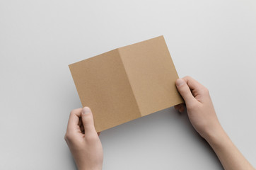 Kraft A6 Bi-Fold / Half-Fold Brochure Mock-Up - Male hands holding a kraft bi-fold on a gray background.