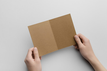 Kraft A6 Bi-Fold / Half-Fold Brochure Mock-Up - Male hands holding a kraft bi-fold on a gray background.